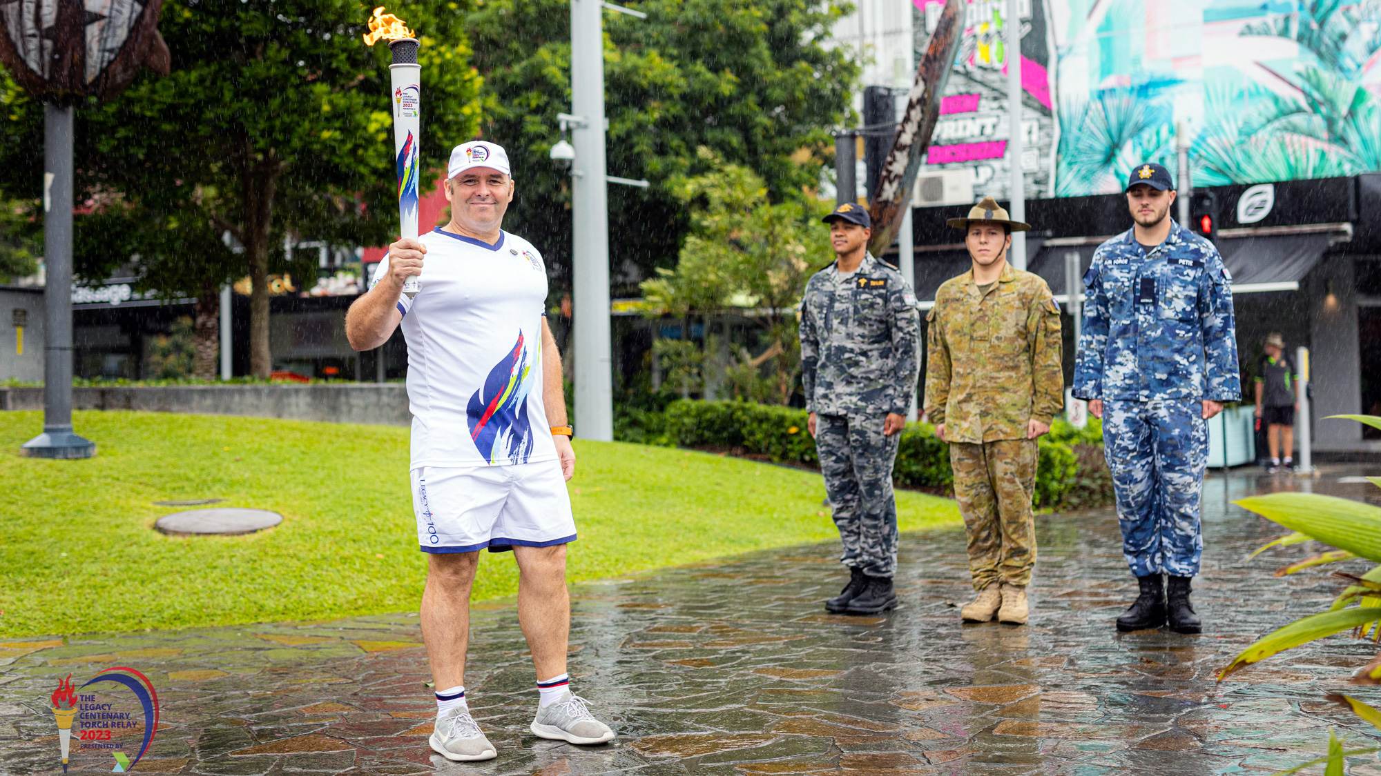 Drew holding torch during Legacy Torch Relay with Army, Navy and Air Force personnel in background