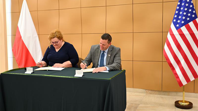 A woman and a man sign an agreement with Wojskowe Zakłady Motoryzacyjne S.A. (WZM) and BAE Systems