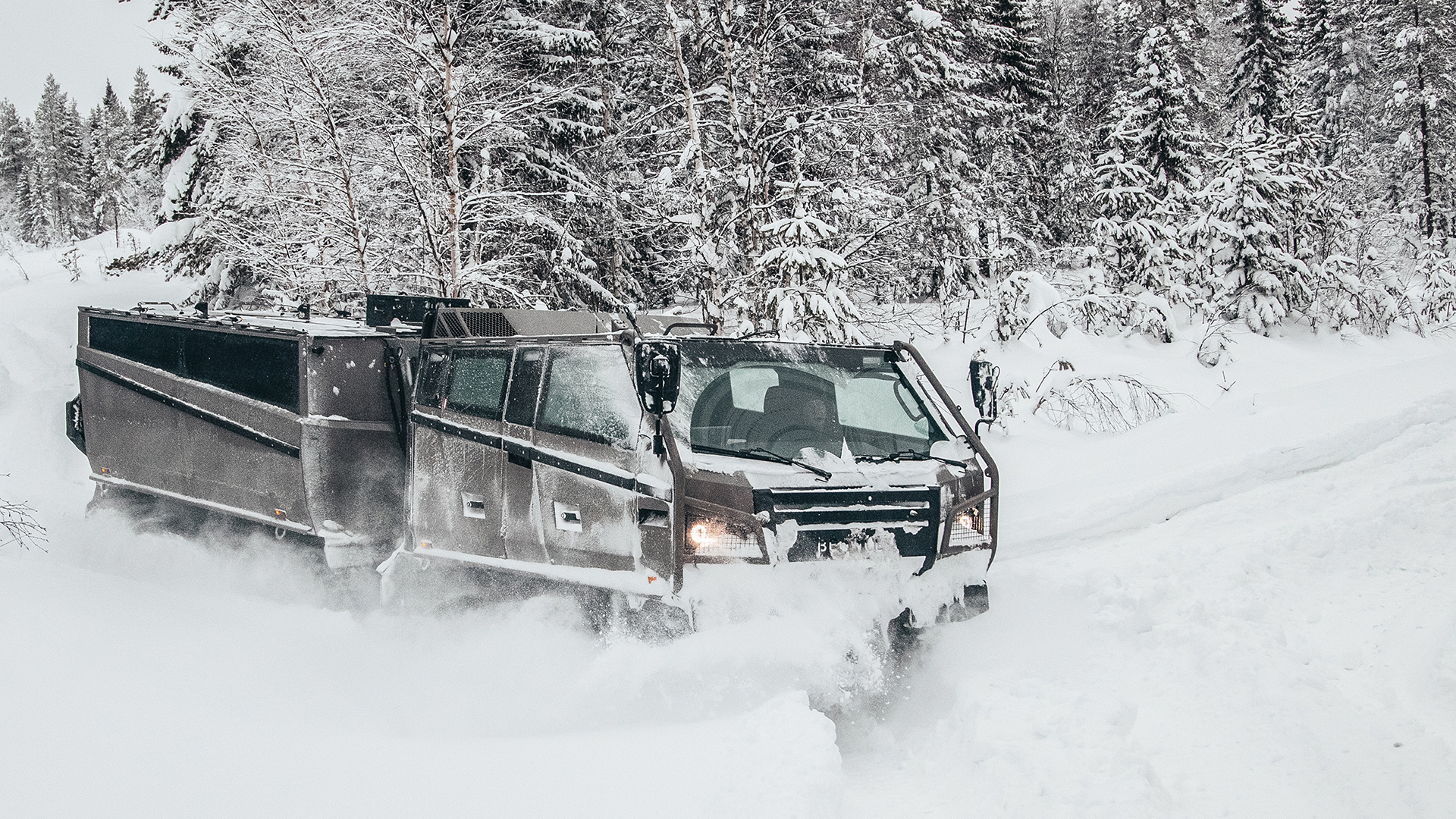 A Beowulf vehicle viewed from the side as it drives through snow-covered woods