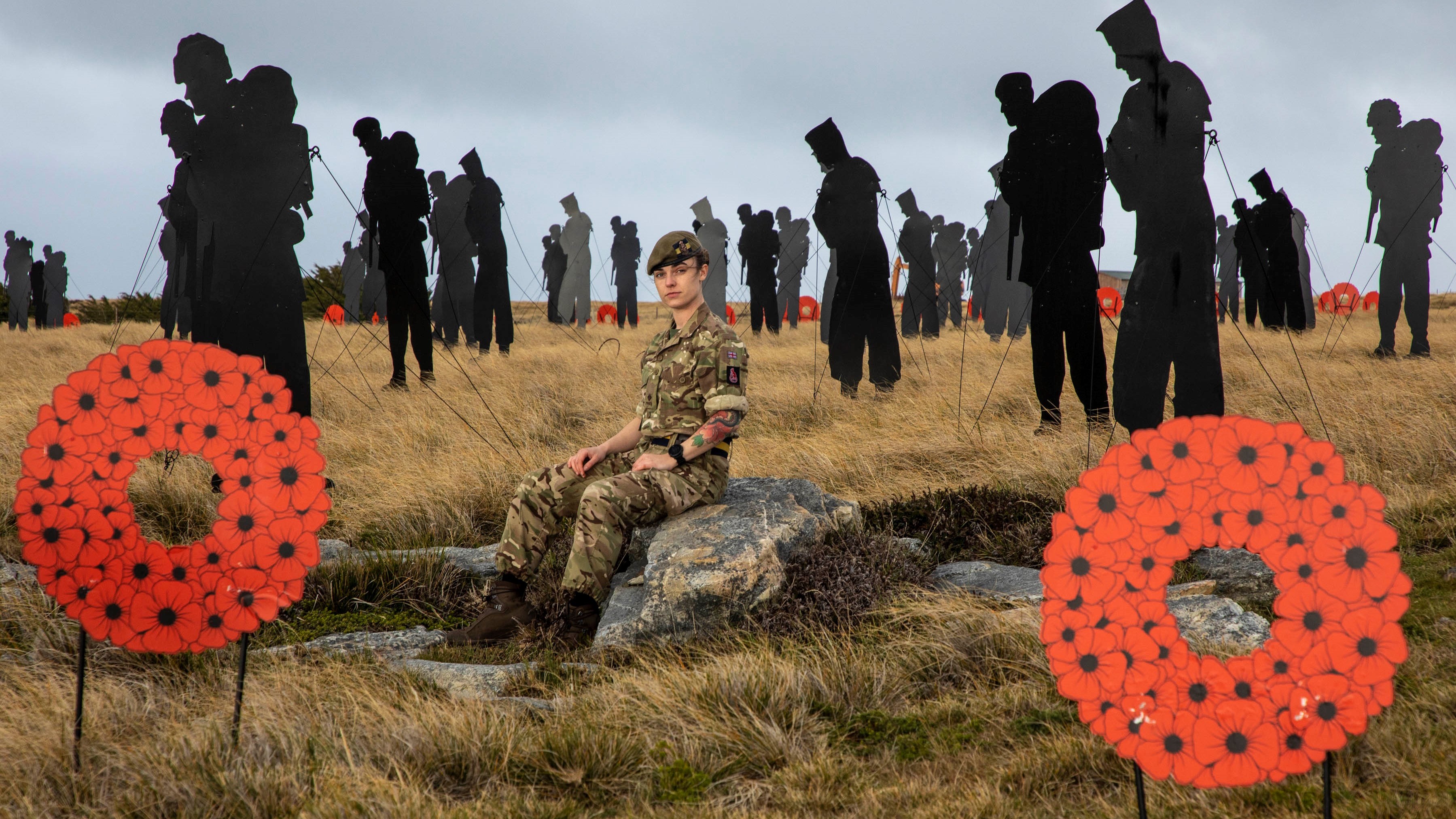 Rhian sat in front of war memorial soldier silhouettes and two poppies