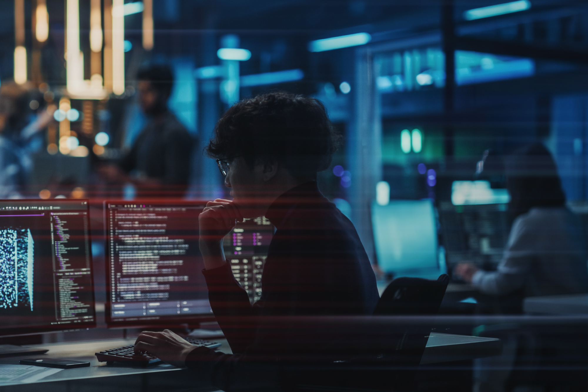 Graphic designed image of a person sitting in front of a computer with lots of data and technology colour flashes