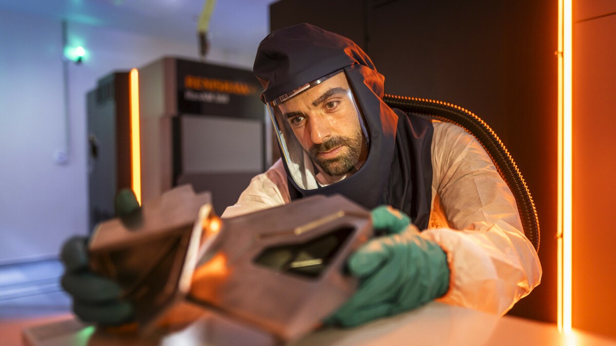 A man in a protective suit reviewing an aircraft part that he has 3D printed