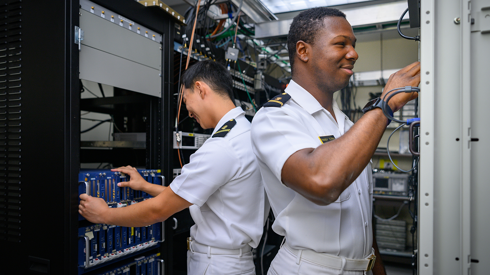 Two U.S. Naval Academy Midshipmen interns working back-to-back in an engineering lab