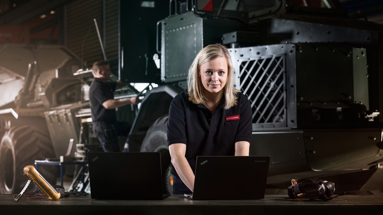 A blonde woman in a BAE Systems shirt works at a laptop