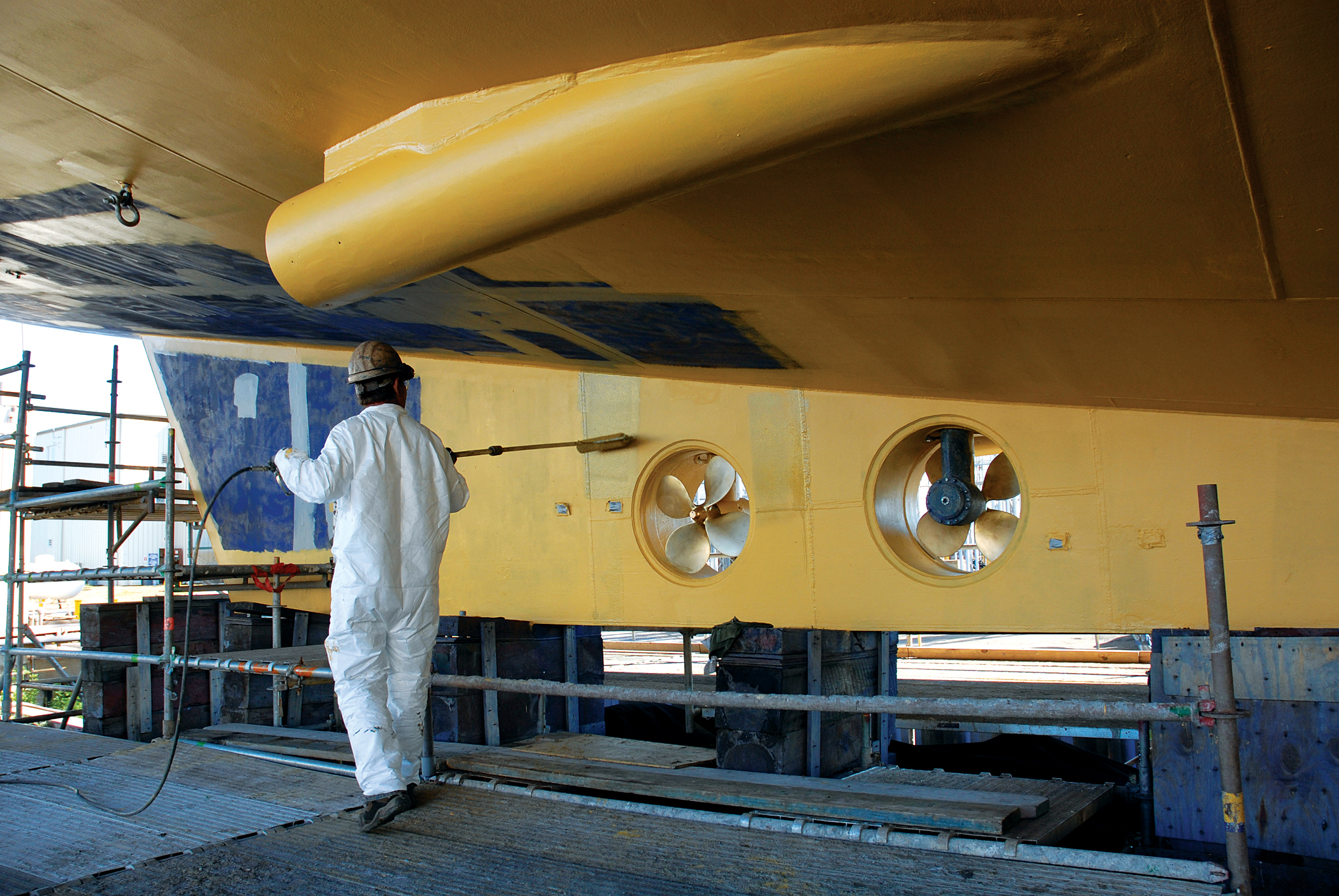 An employee painting a yellow side of a ship