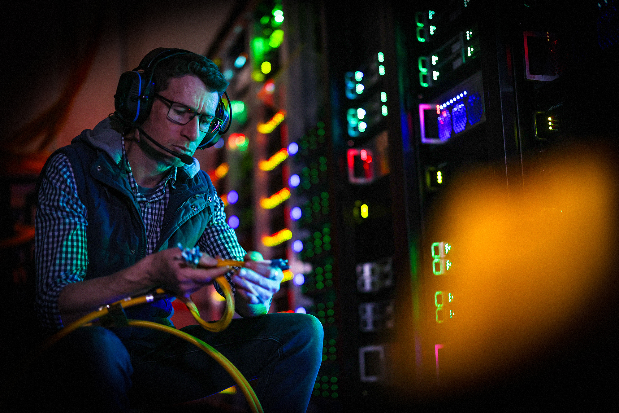 Man in lit up server room wearing headset and holding cables