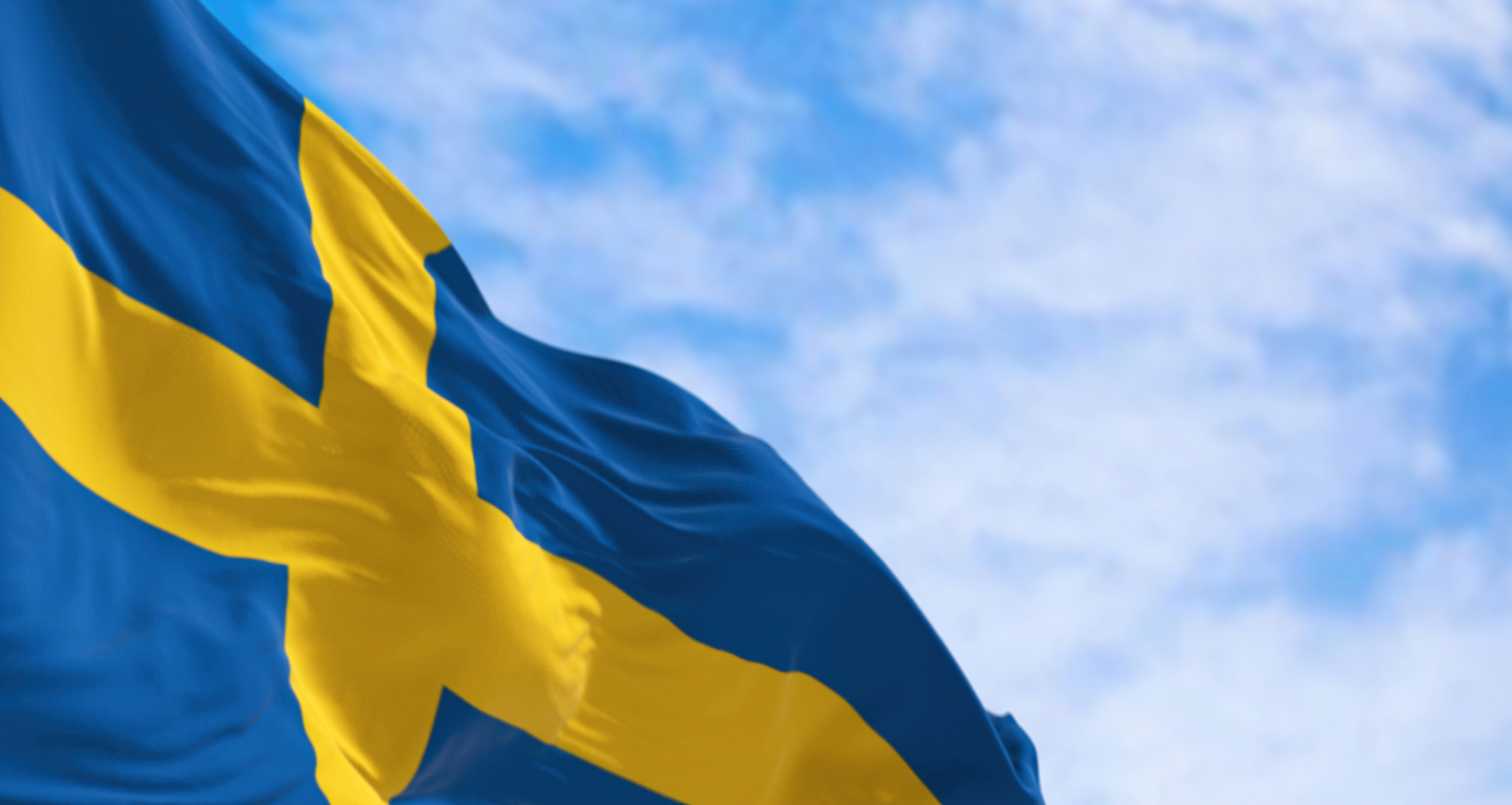A Swedish flag waves in the sky on a cloudy day