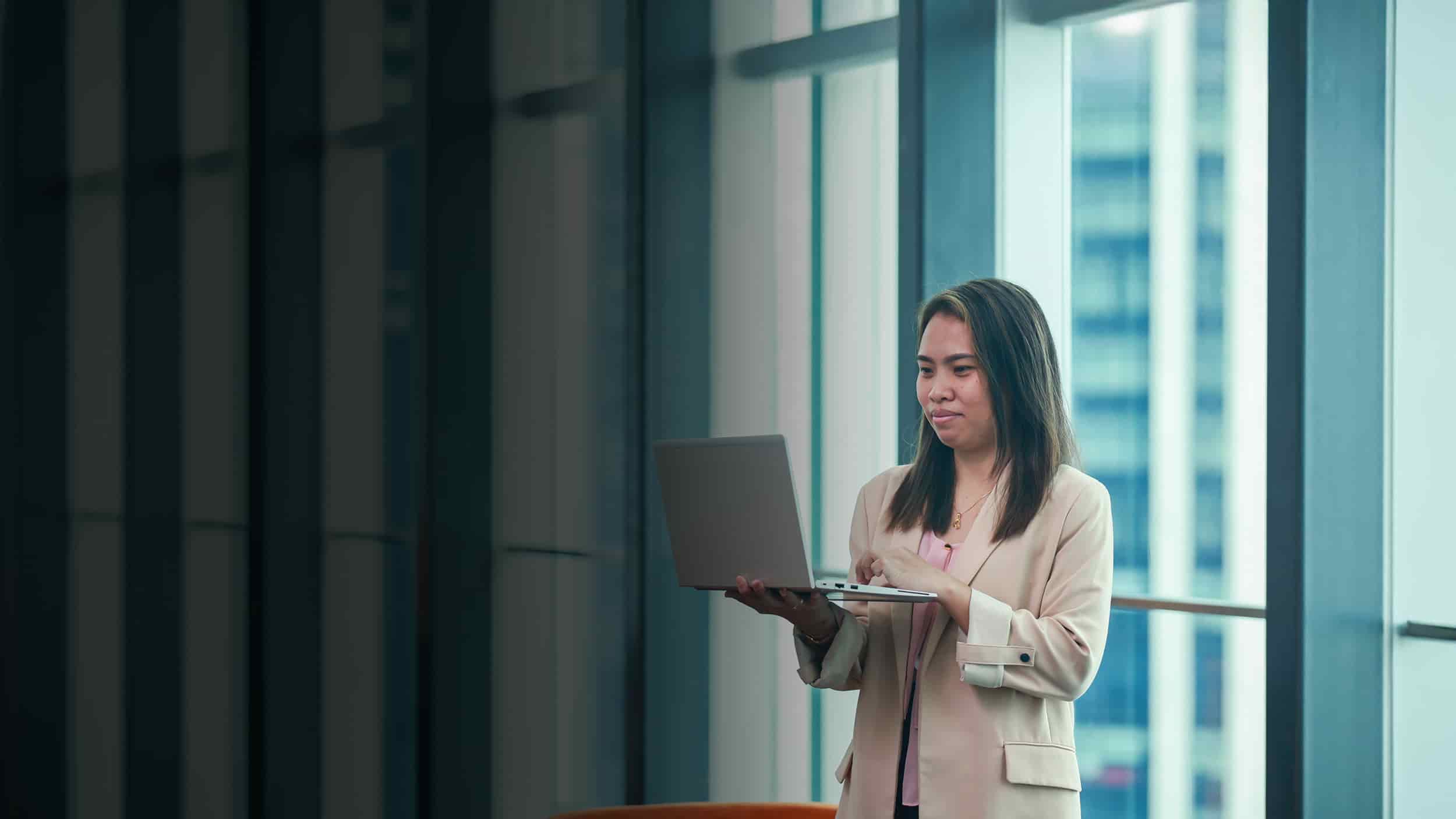 Woman consulting laptop in front of a glass wall
