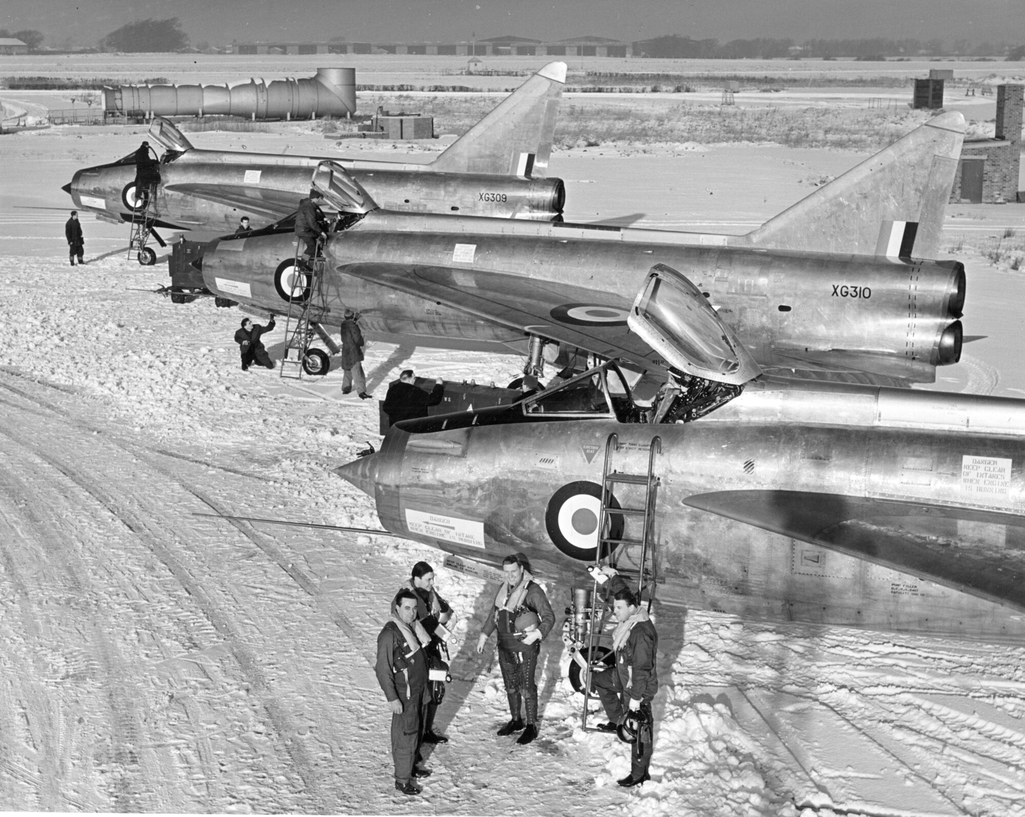 English Electric Lightning P1B - three aircraft lined up at a snowy Warton with pilots alongside.