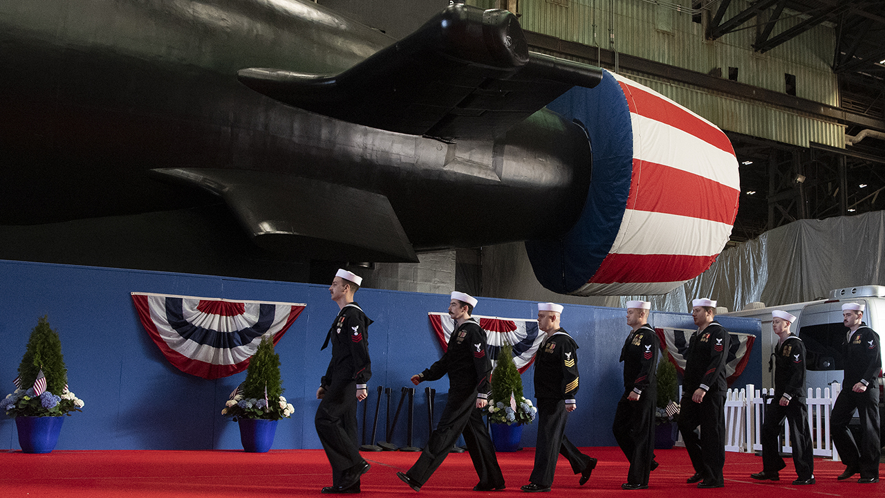 U.S. Navy sailors parade past a covered submarine propulsor at an event