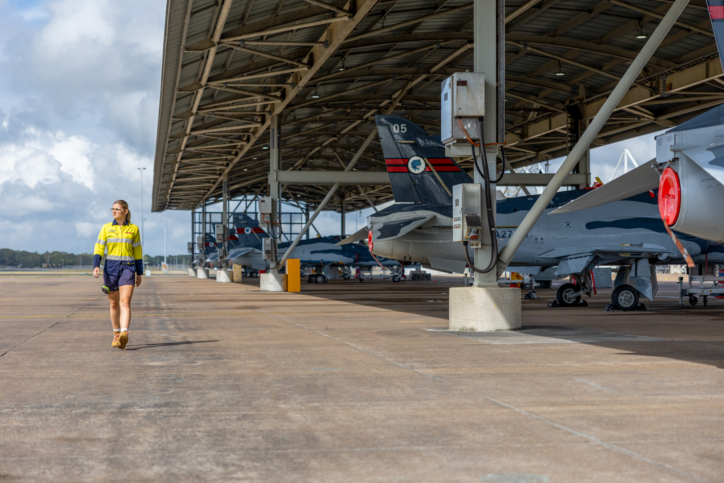 Avionics technician walking alongside a hanger full of Hawk Lead-in Fighter aircraft, on a sunny day in Williamtown