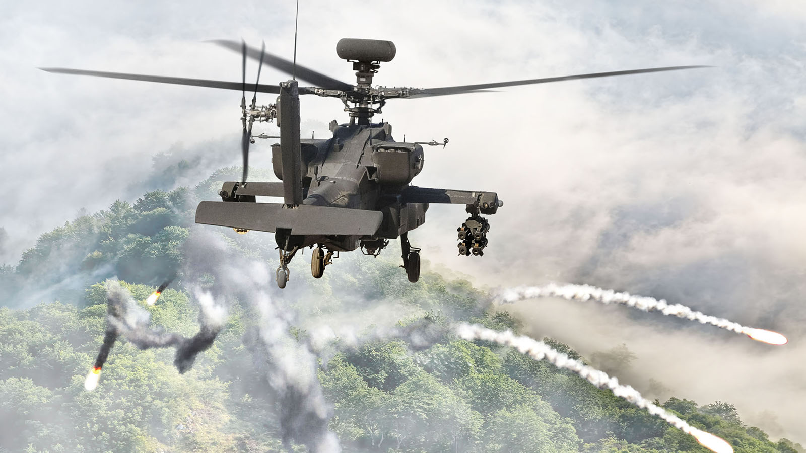 An Apache helicopter fires flares in self-defense. Fog hovers over a dense forest below.