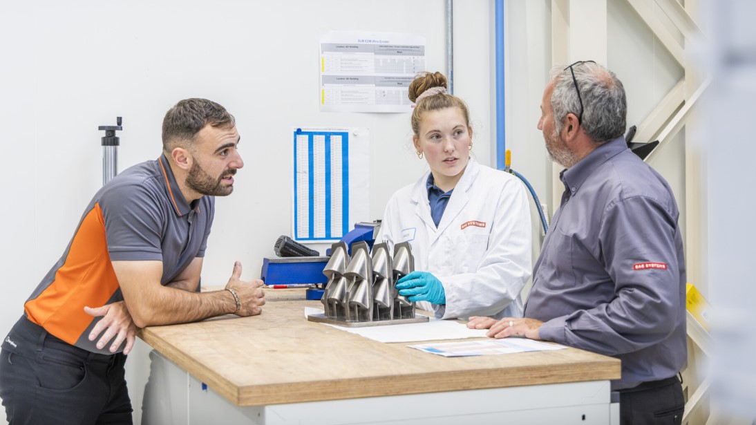 Three BAE Systems employees discussing an additive manufacturing project in an operational environment. 