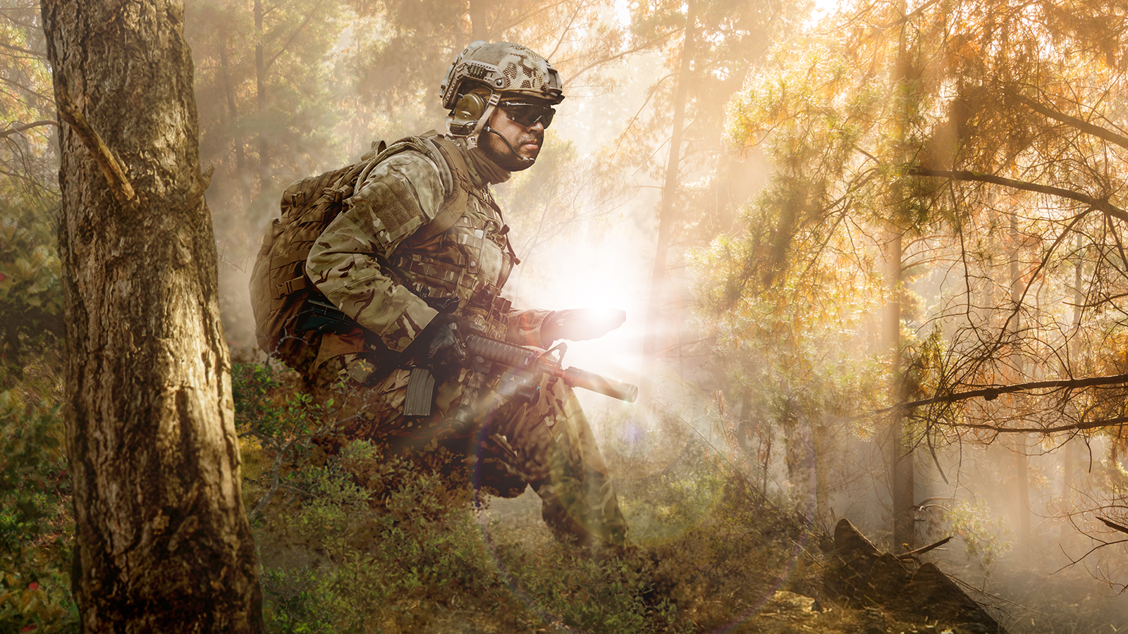 Soldier wearing camo gear carrying rifle and backpack traveling through dense forest with sunshine rays in background. 