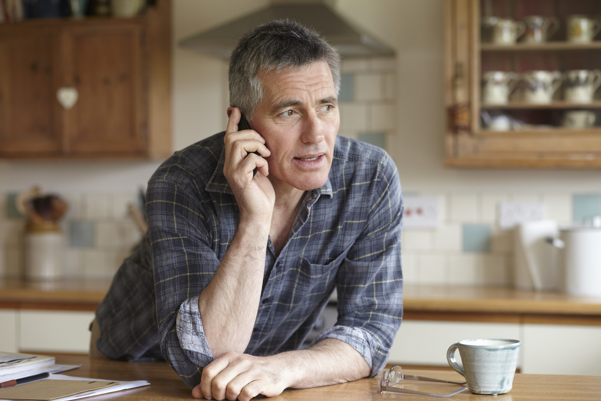 Man uses phone leaning against kitchen worktop