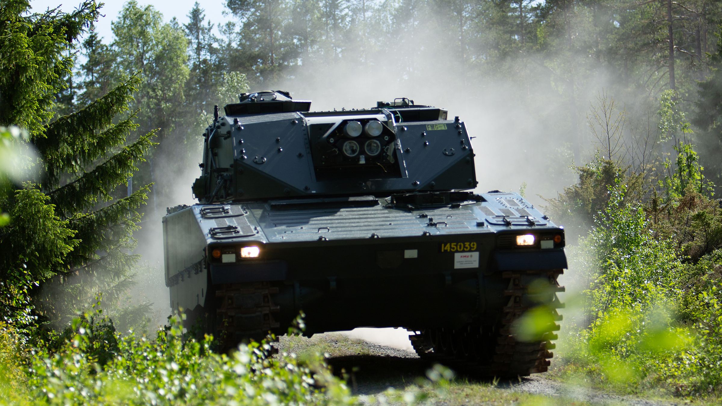 A black CV90 Mjolner drives through a forest with a dust cloud behind it