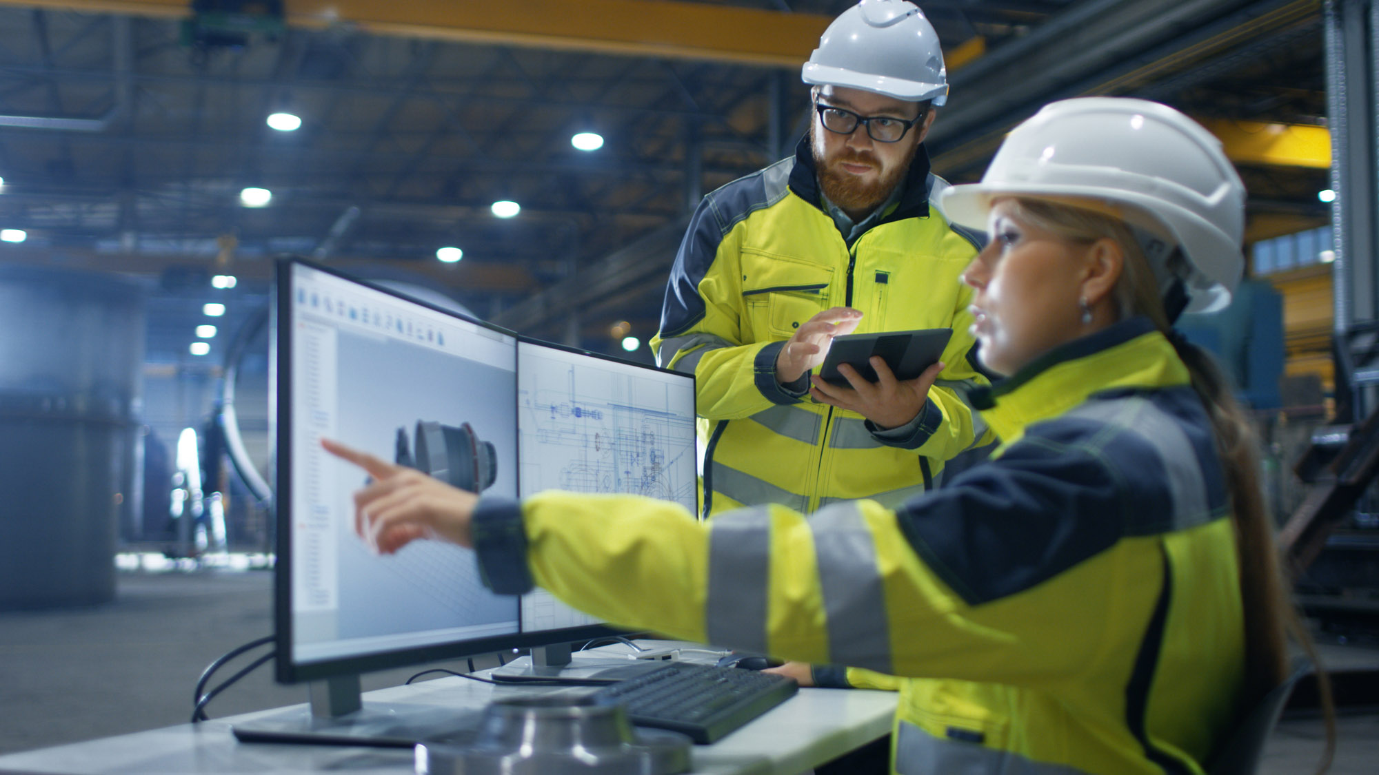 Heavy Industry Factory Female Industrial Engineer Works on Personal Computer, Her Male Colleague Talks with Her and Uses Tablet Computer