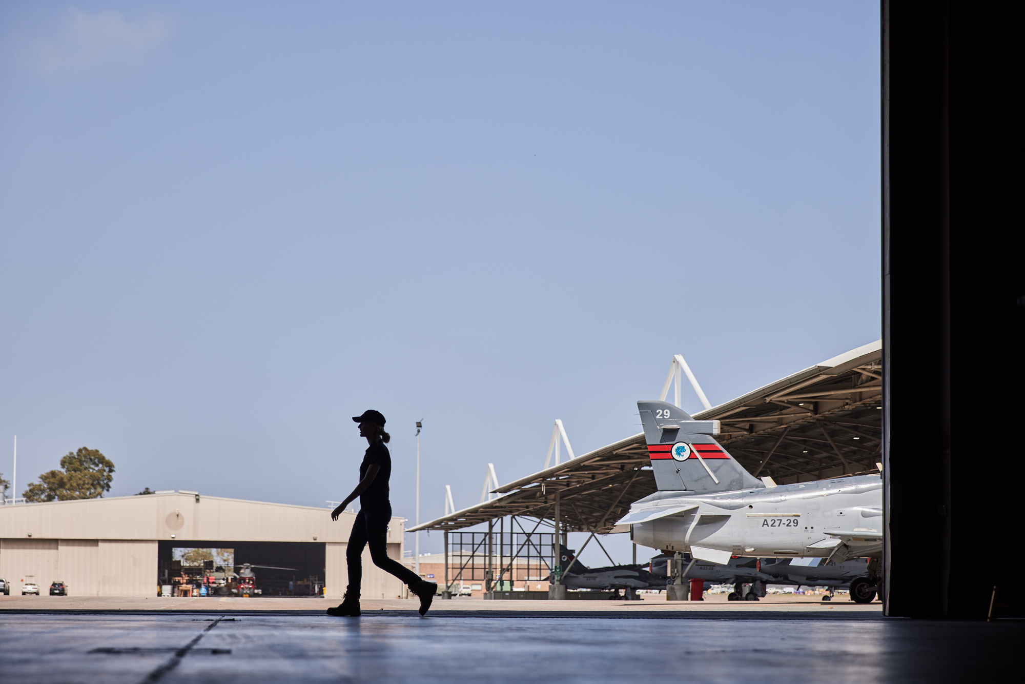 Female apprentice walks right to left across Williamtown Hawk LIF hanger