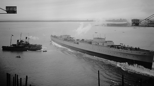 Cruiser, HMS Ajax (Leander class). Launched into Walney Channel - starboard view with tugs, including Cartmel in attendance, 1st March 1934. Credit: The Dock Museum, Barrow-in-Furness