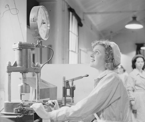 Everyday life at a munitions factory, UK, 1941. Miss R Higginbotham operates a press for fuse detonators at a munitions factory, somewhere in Britain. Credit: IWM.