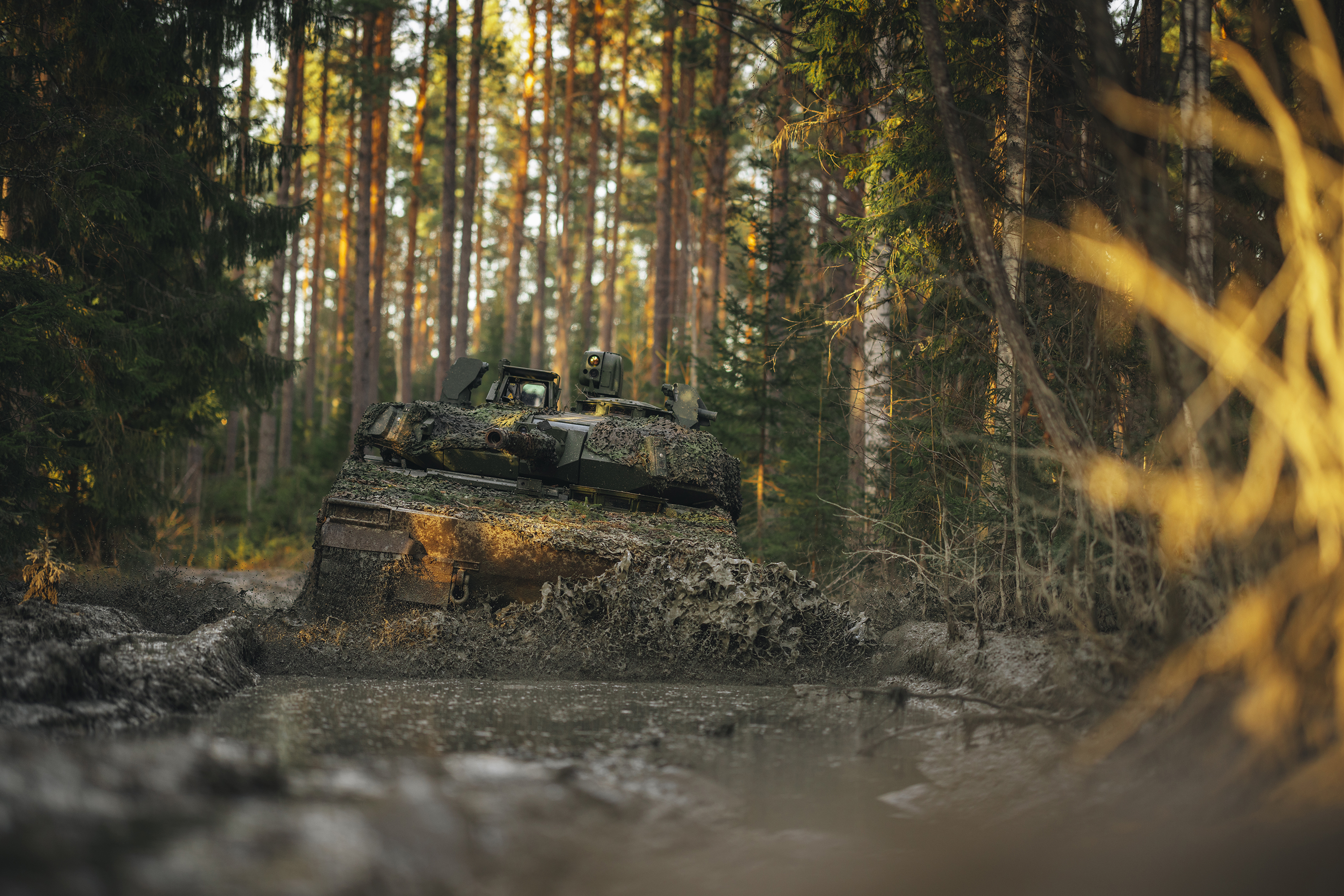 CV90 Infantry Fighting Vehicle driving through muddy terrain in a forest