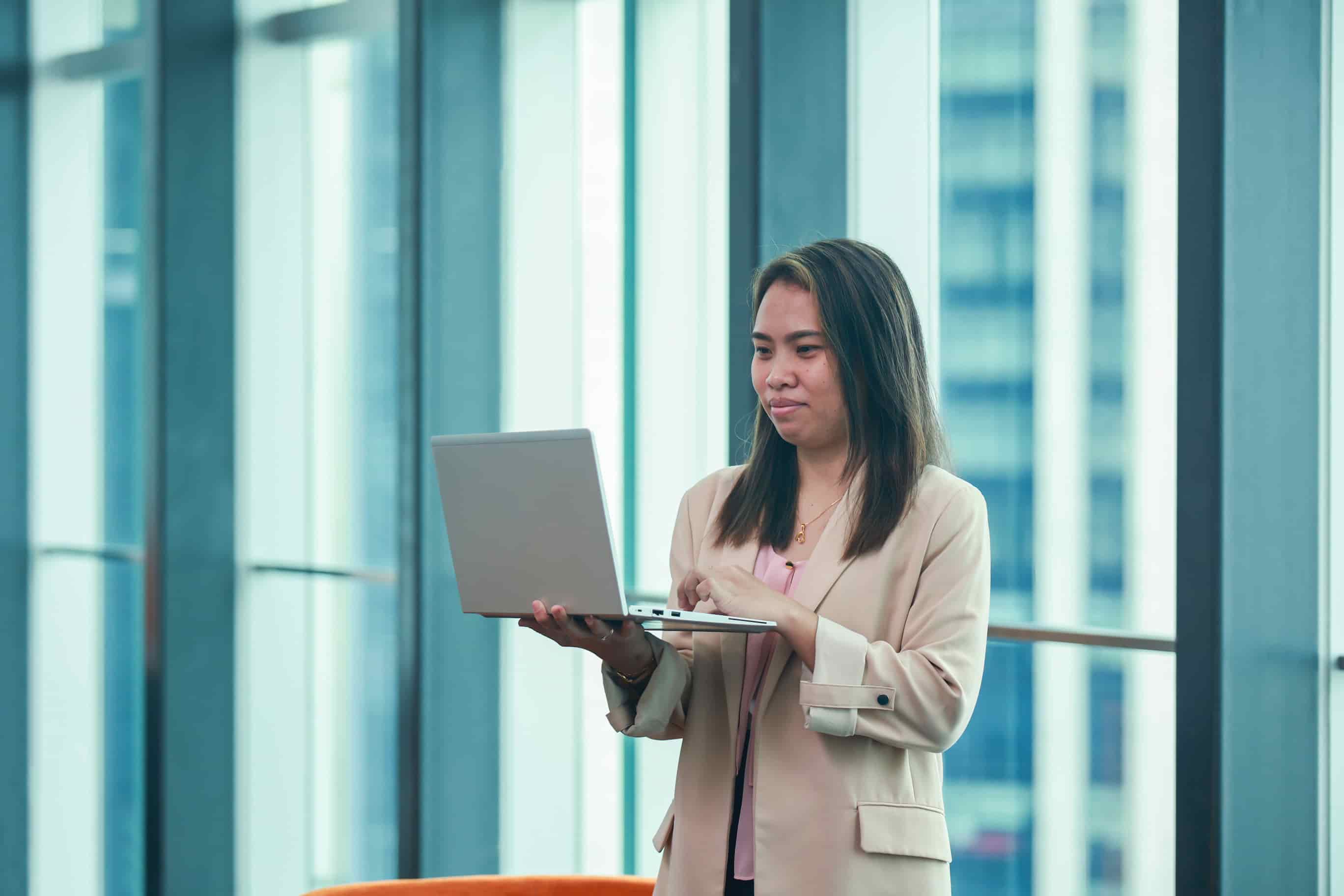 Woman standing before a glass wall peering at laptop