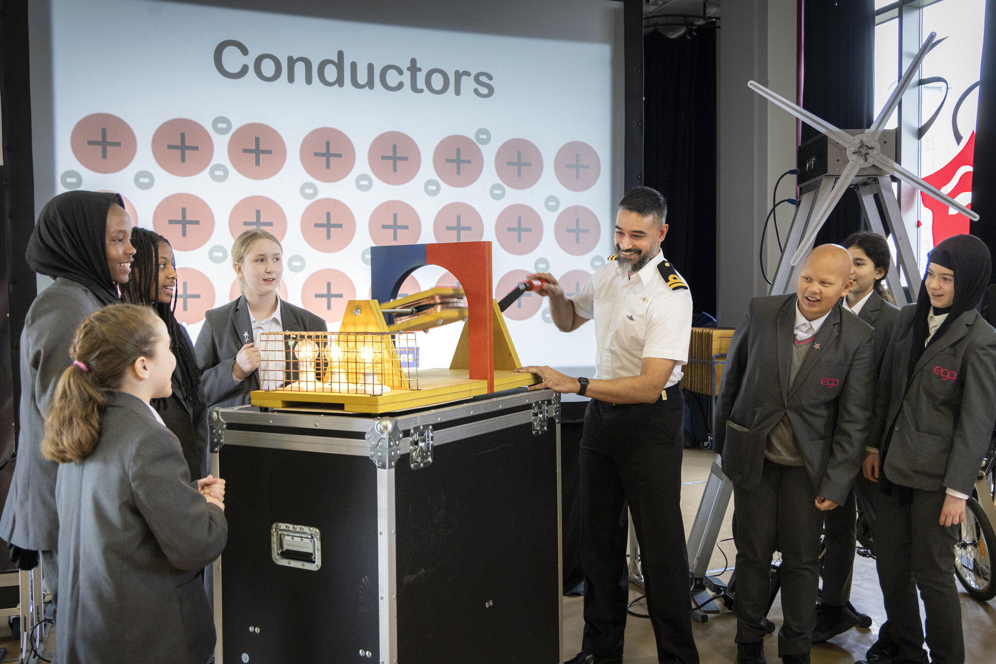 A Royal Navy Officer demonstrates an interactive science experiment with a group of school students during BAE Systems' nationwide STEM theatre show 