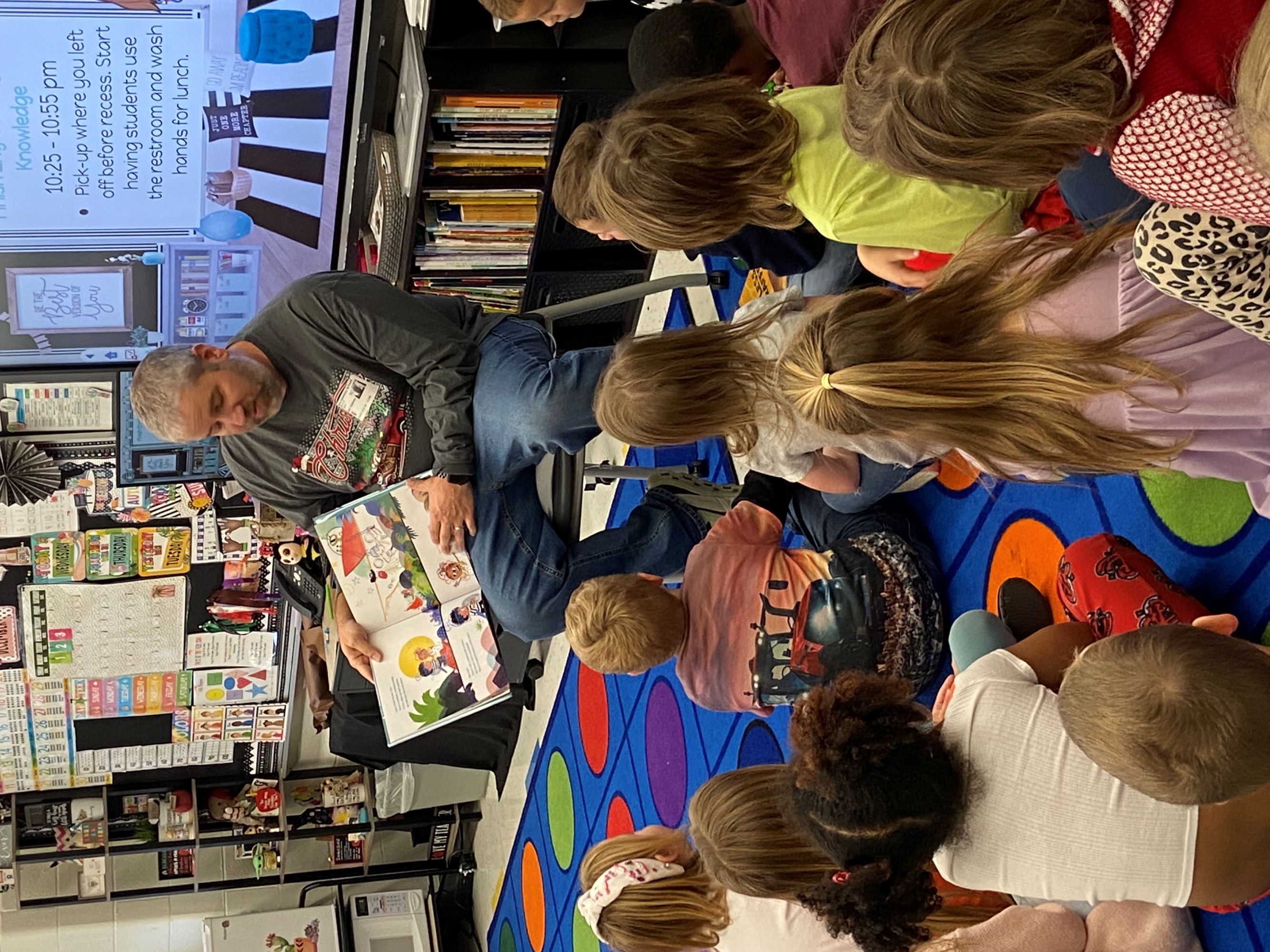 A BAE Systems employee reading a book to elementary school students in an animated way.