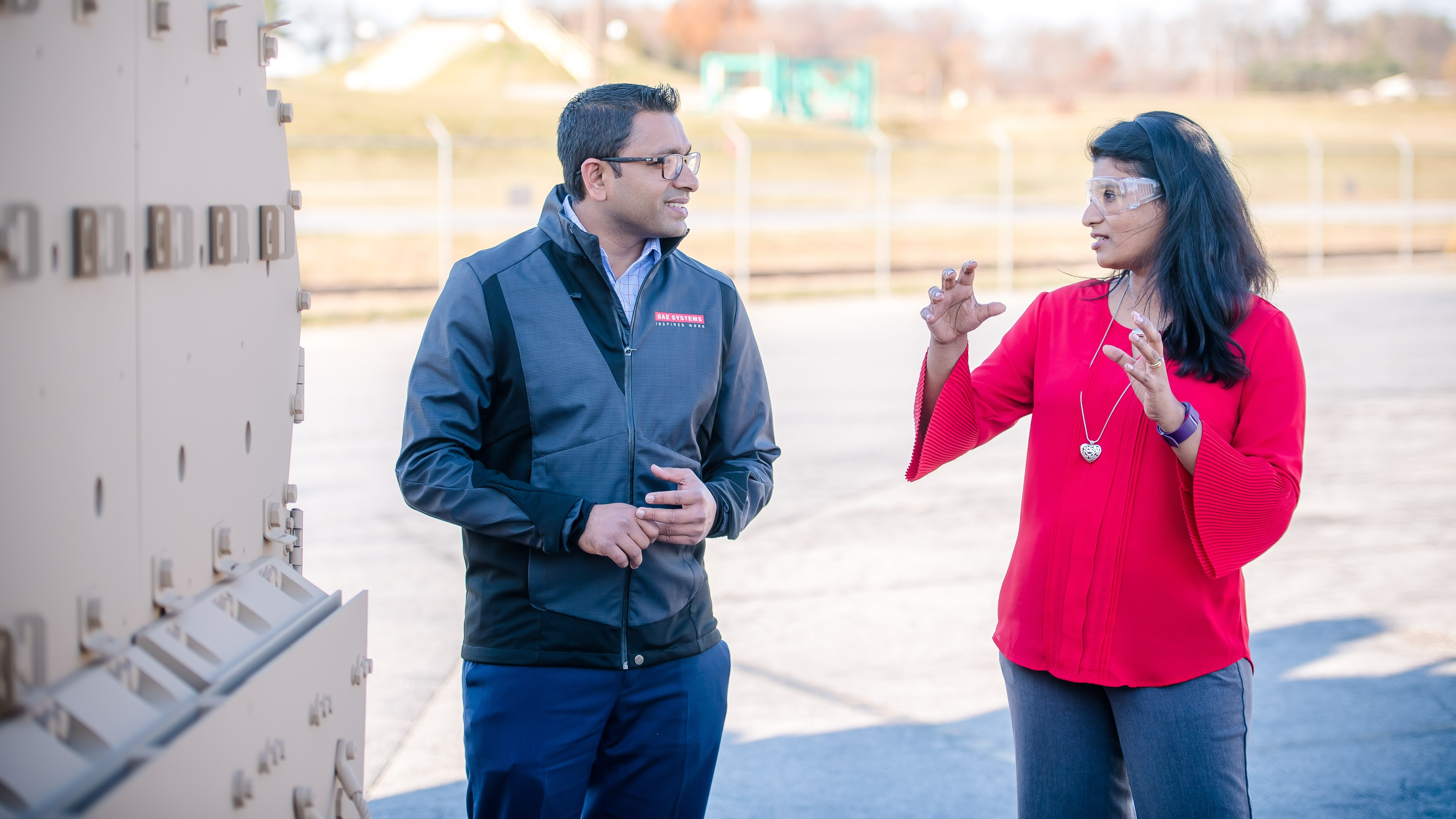 A woman wearing eye protection explains a concept to a man wearing a BAE jacket