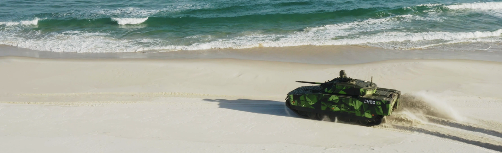 A green CV90 drives on a beach in Brazil