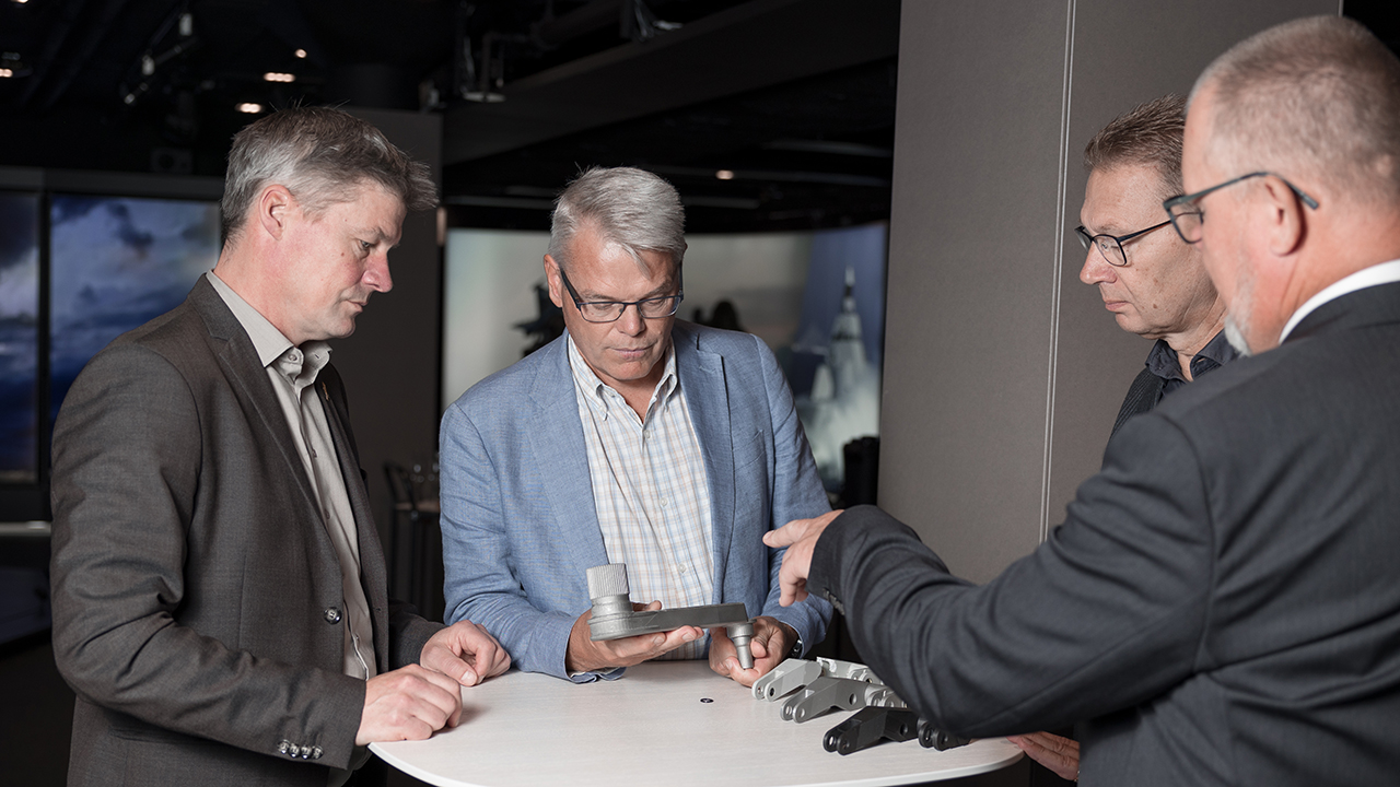 Saab and BAE Systems employees in a group around parts created using additive manufacturing