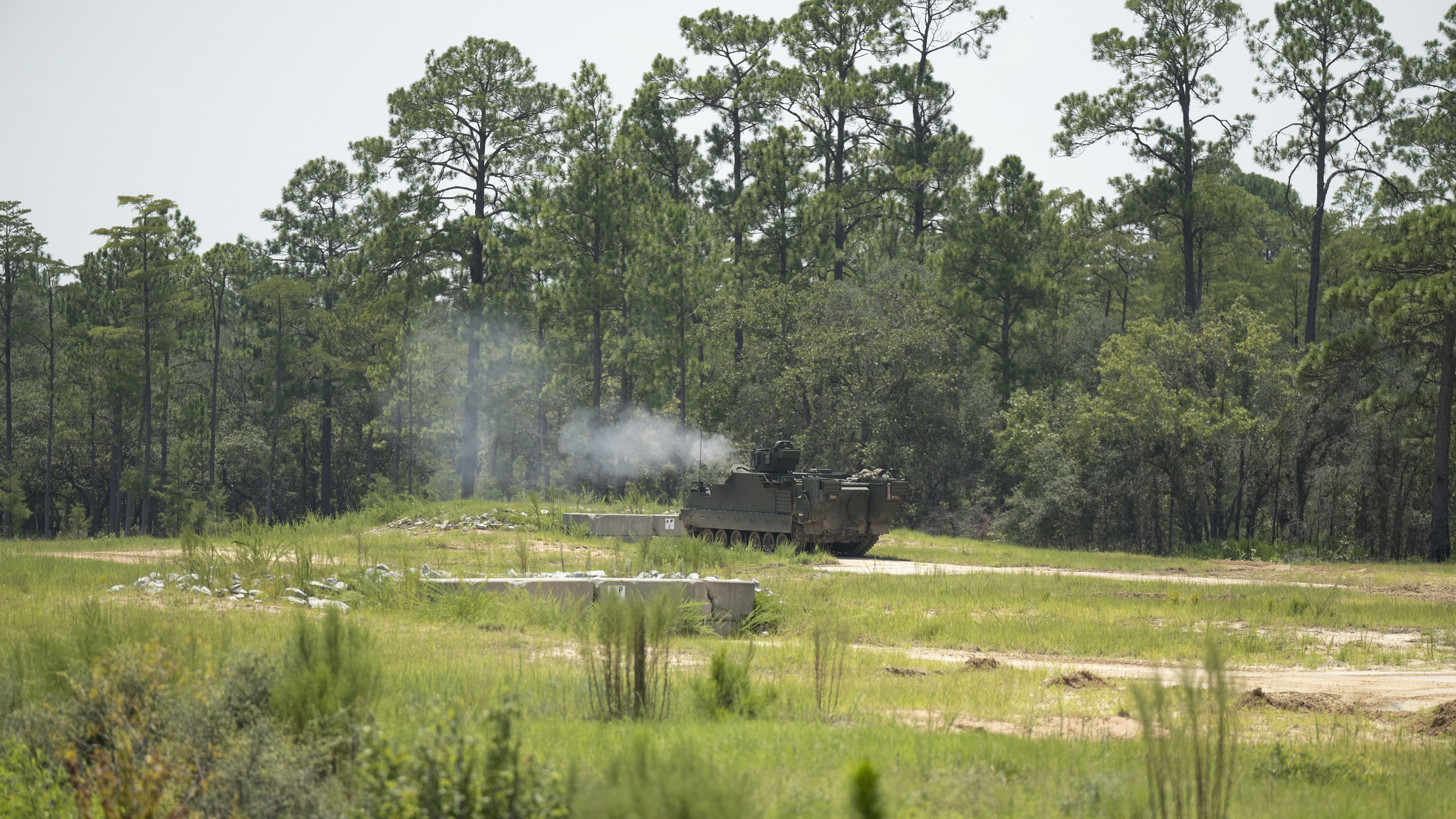 A green AMPV after firing in a field with woods in the background