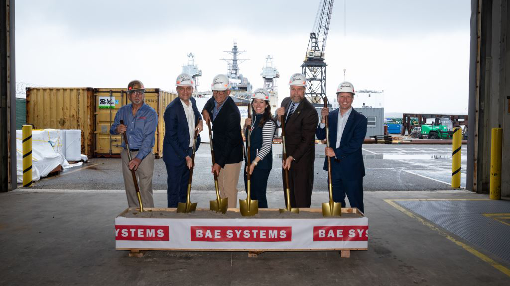Six people stand with shovels and hard hats