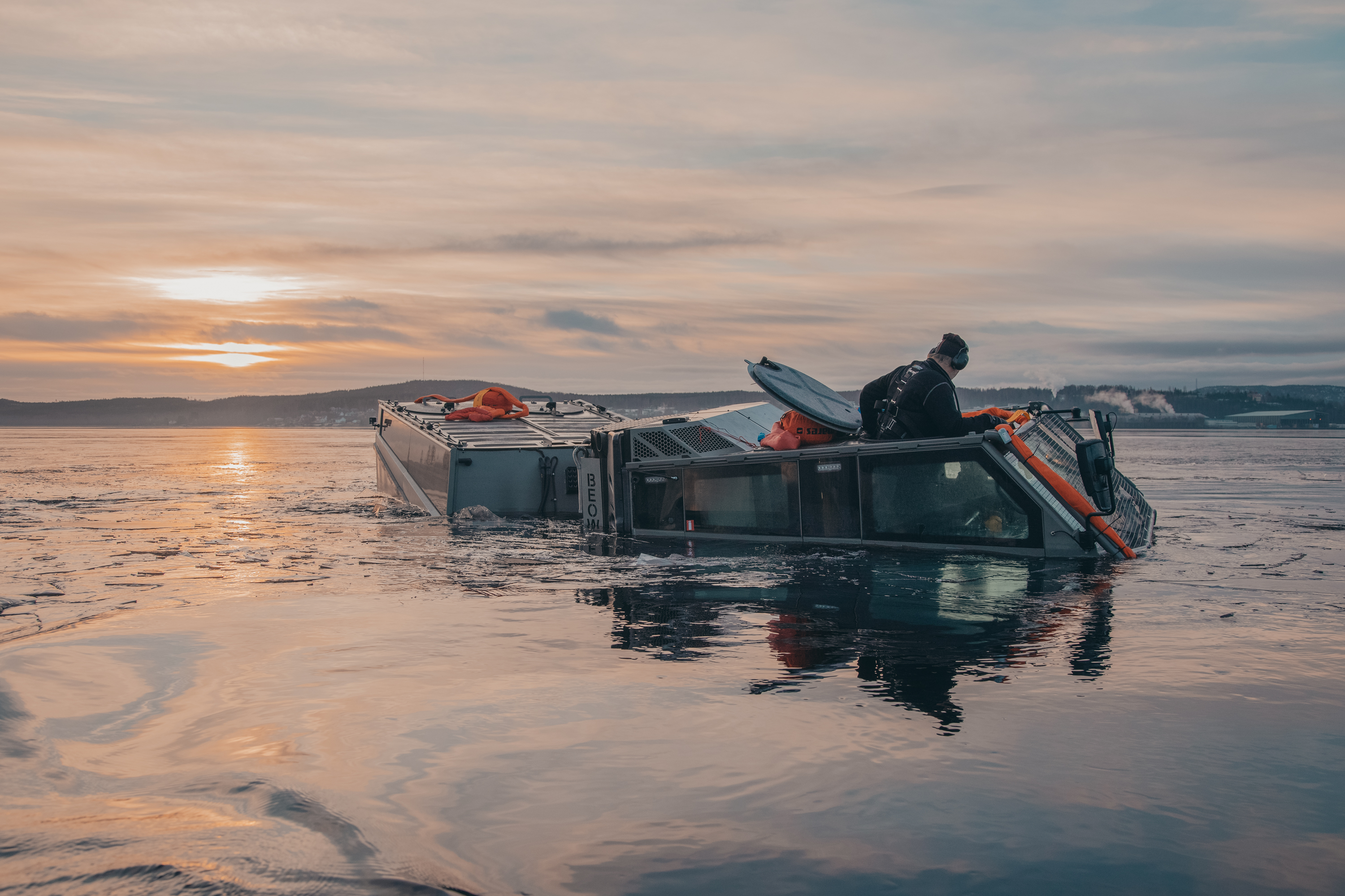 Person in a BvS10 vehicle in water at sunset