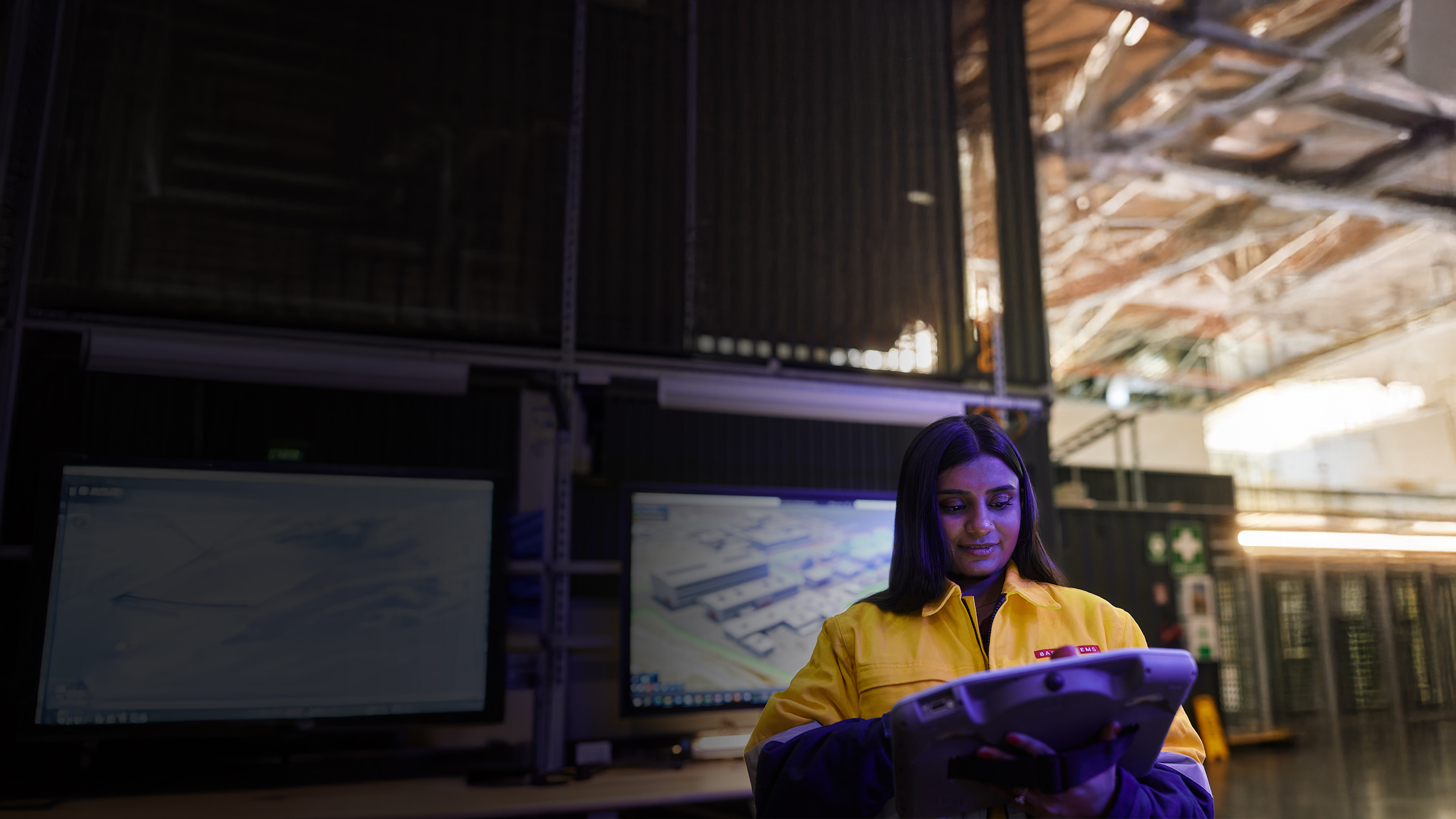 A smiling employee at BAE Systems Australia in front of a bank of computer screens