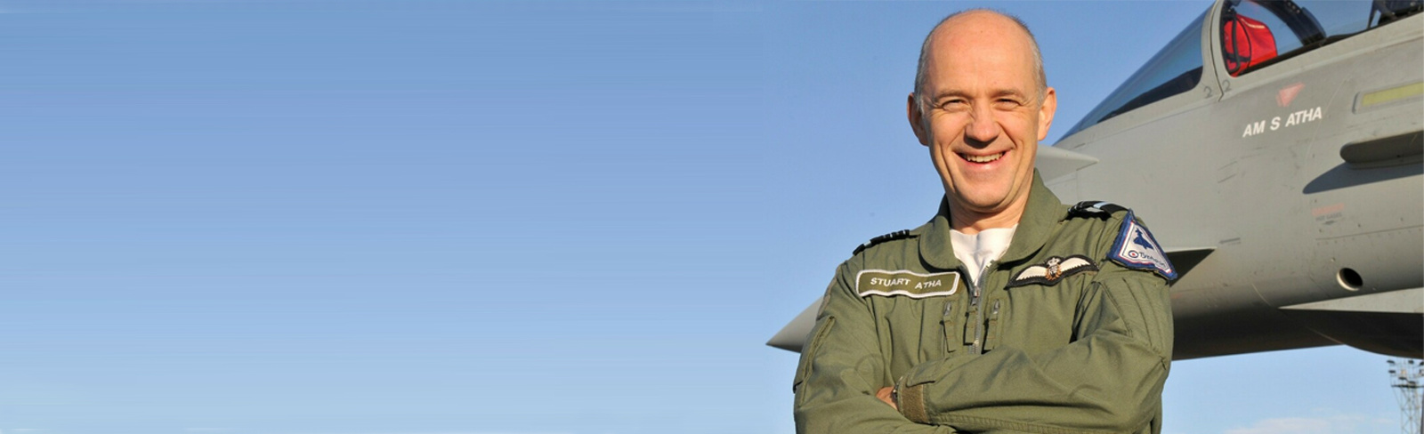 Sir Stuart Atha, Director of Training Strategy, stands next to a Eurofighter Typhoon jet with his arms folded, smiling at the camera.